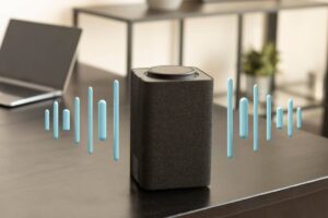 Smart speaker on a desk with visual sound waves, beside a laptop in a modern room.