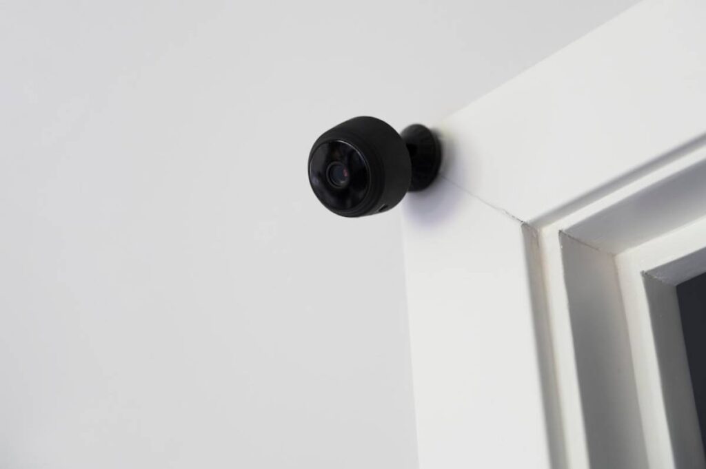 A small black security camera mounted on a white wall near the ceiling.