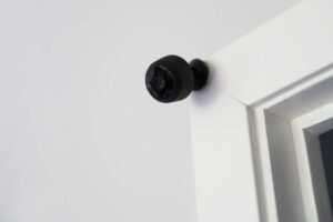 A small black security camera mounted on a white wall near the ceiling.