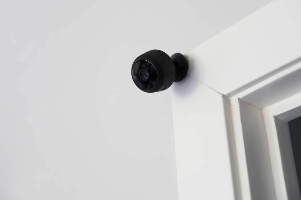 A small black security camera mounted on a white wall near the ceiling.