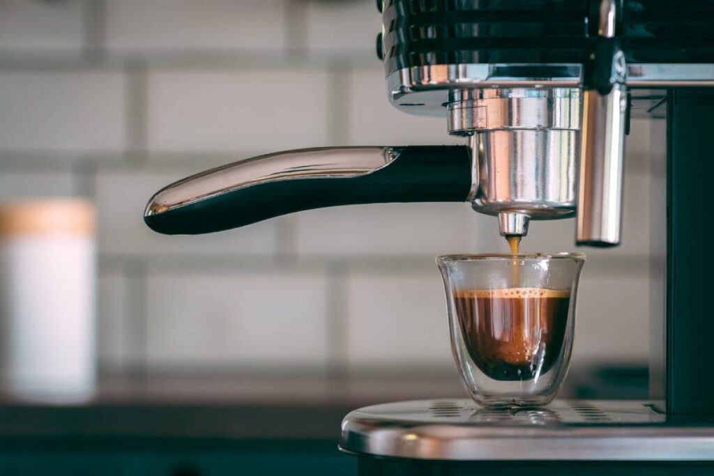 Espresso pouring from a machine into a clear glass cup in a kitchen.