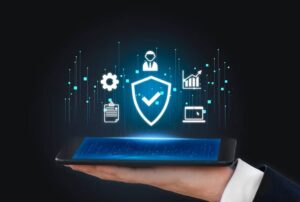 A hand holding a tablet displaying futuristic cybersecurity and business icons holographically, against a dark background.