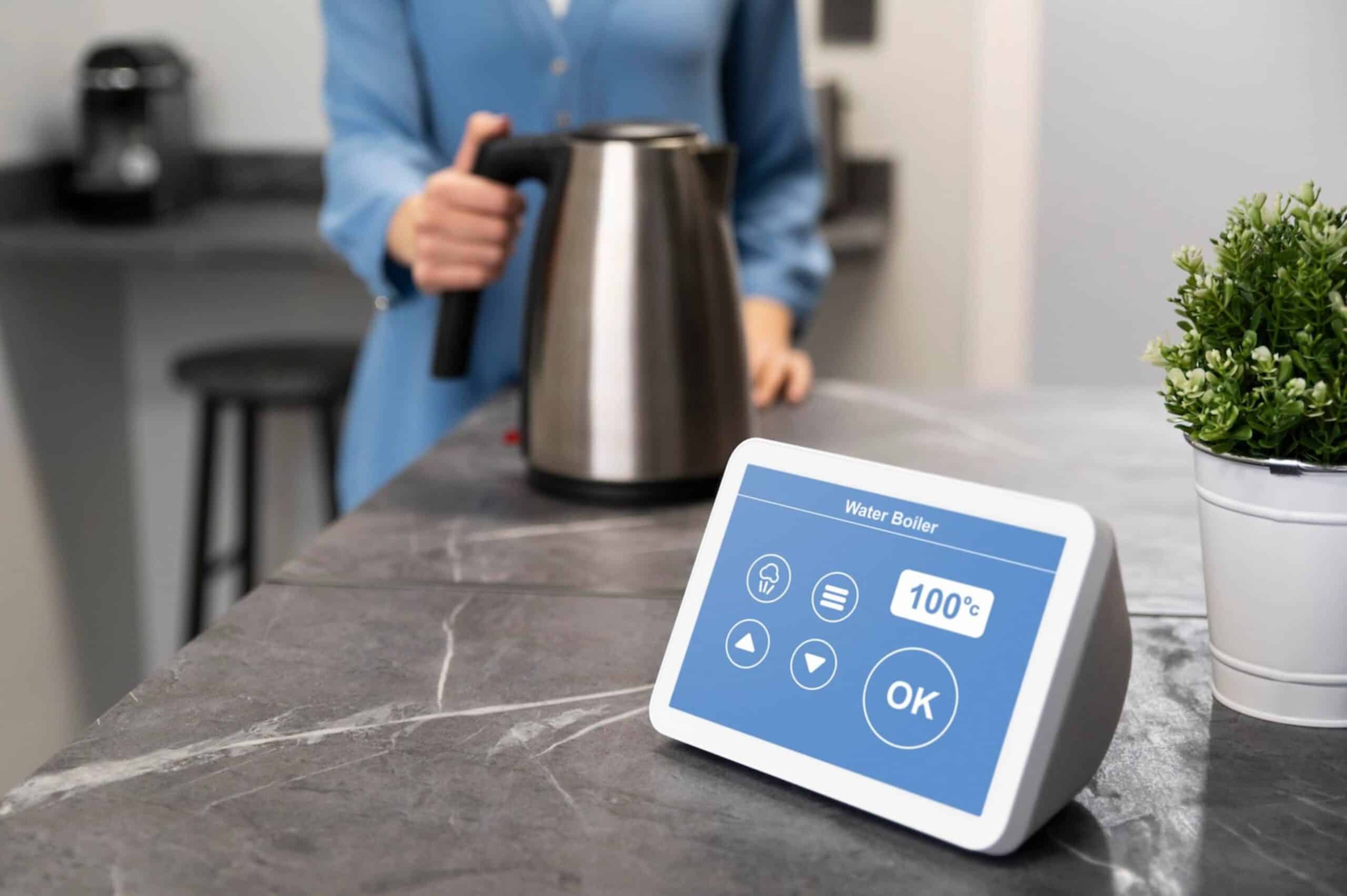 Woman in a blue suit using a stainless steel kettle with a digital display showing temperature on kitchen counter.