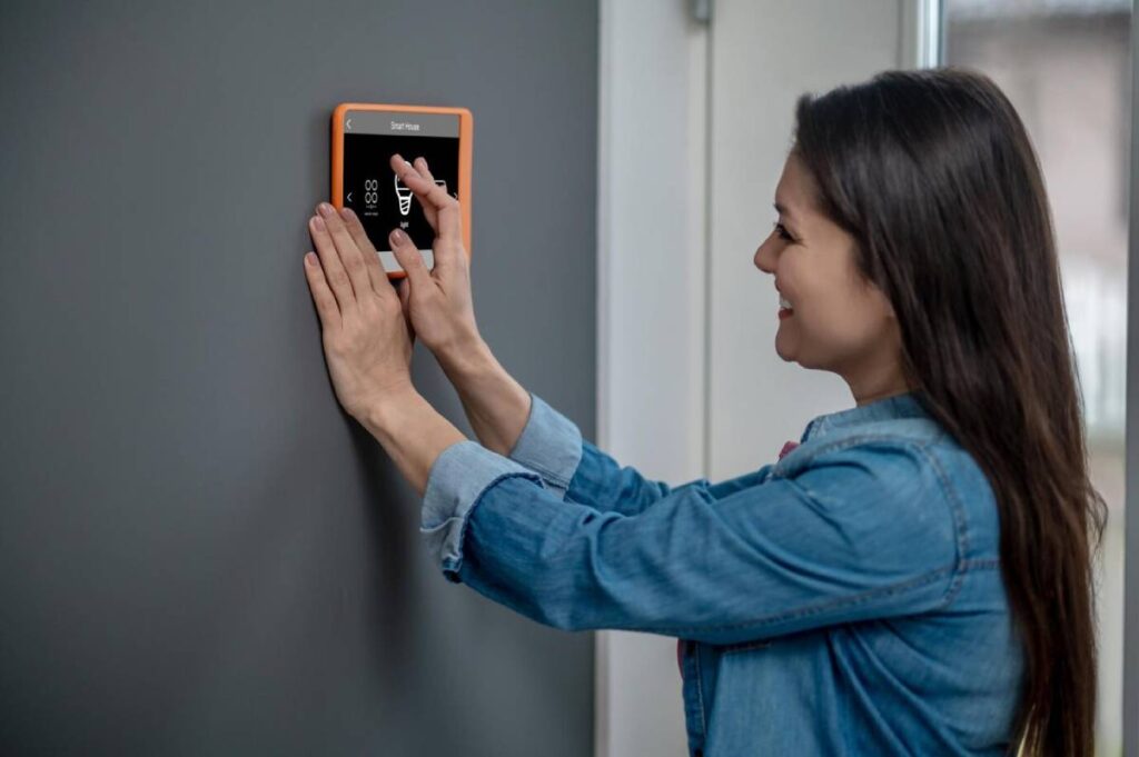 A woman holds an orange smart device, looking engaged and focused on its screen.