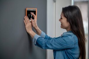 A woman holds an orange smart device, looking engaged and focused on its screen.