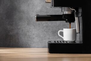 Espresso machine pouring coffee into a white cup on a wooden table against a grey background.