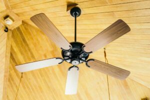 A ceiling fan with wooden blades mounted on a wooden ceiling, viewed from below.