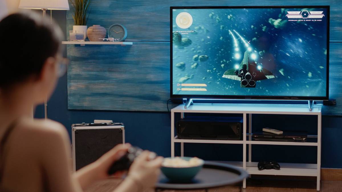 Person playing a space-themed video game on a large TV in a modern living room.