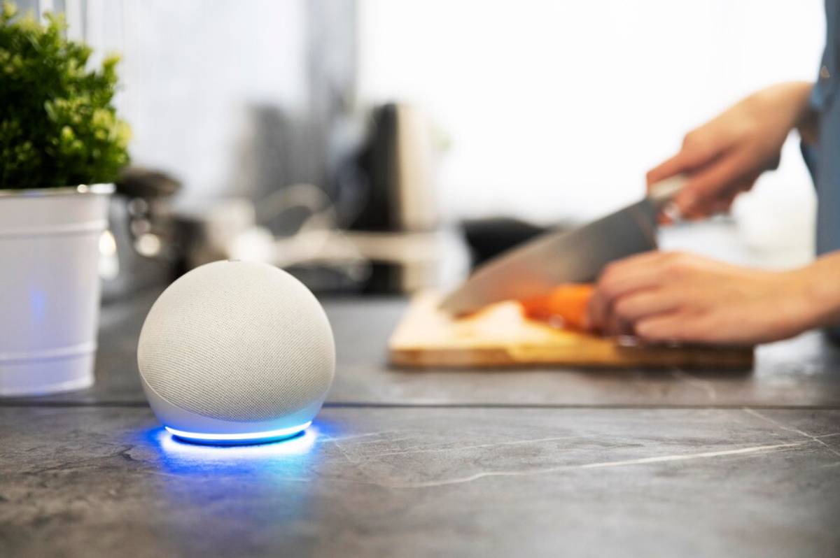 Smart speaker on kitchen countertop lit up, with person cutting vegetables in the background.