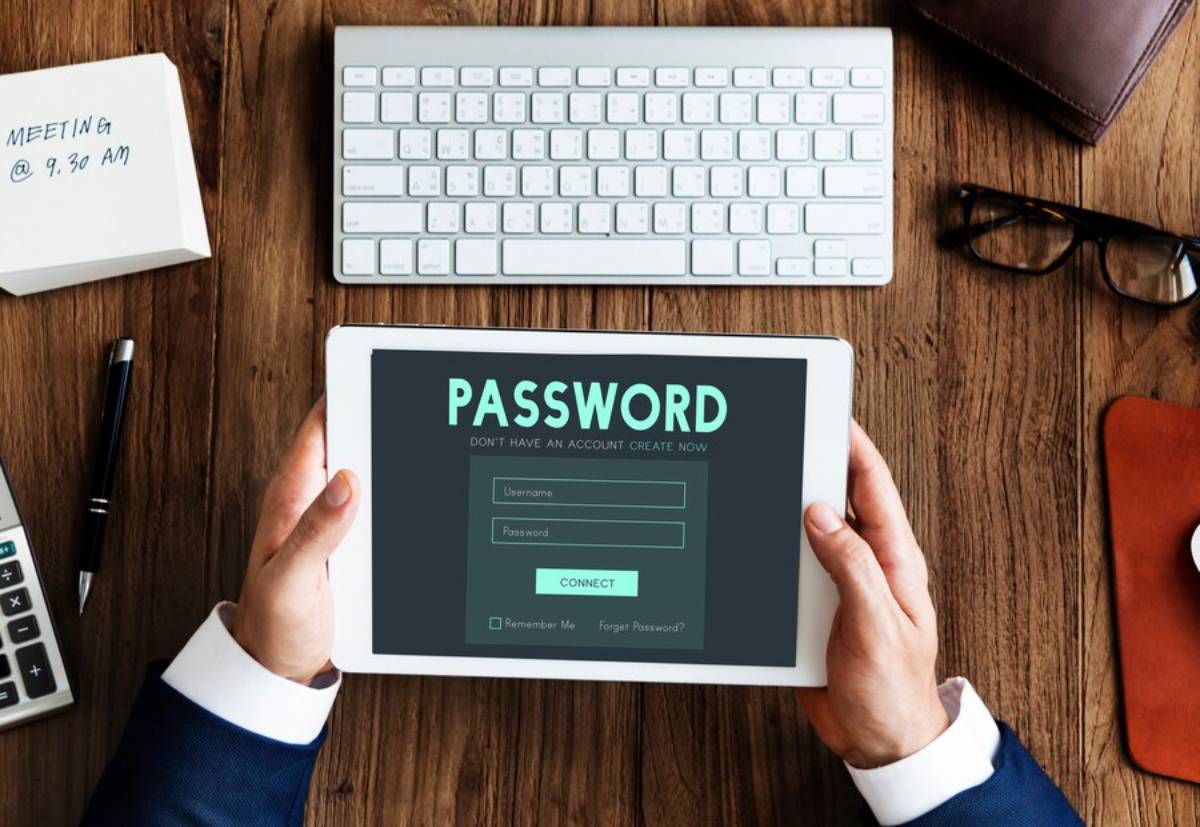 Person holding a tablet showing a password login screen, with a keyboard and office items on a wooden table. 