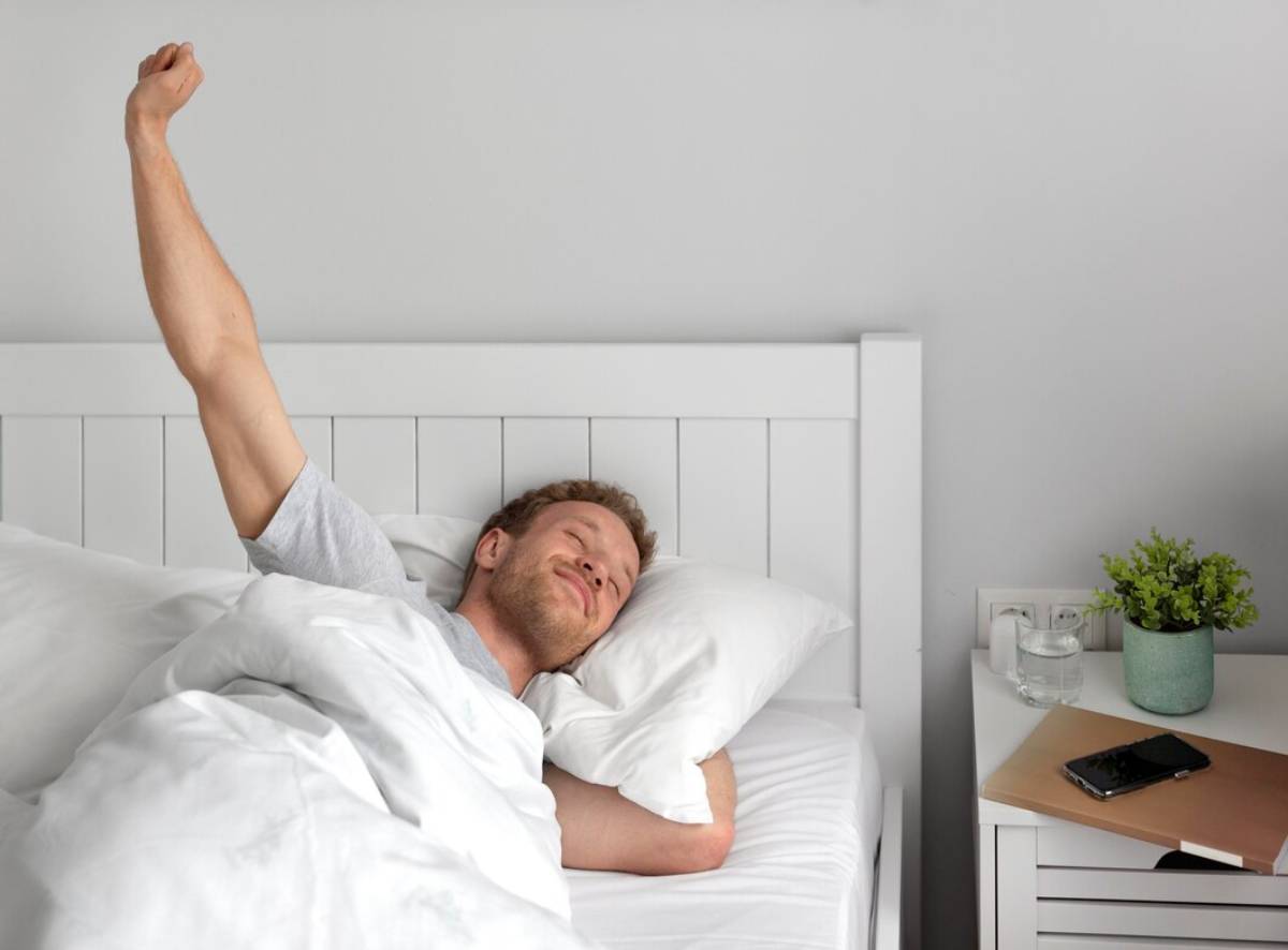 A man stretching while lying in bed, looking relaxed and content. 