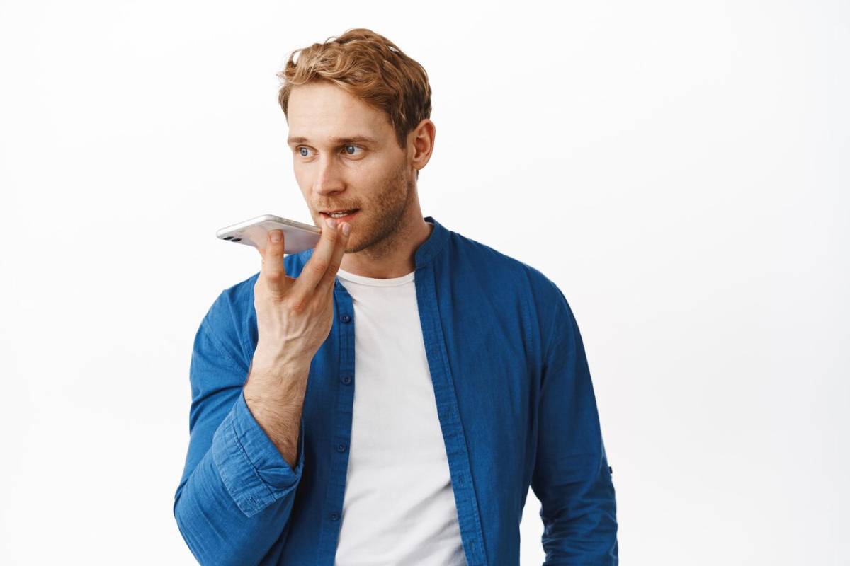 Young man in blue shirt using voice assistant on smartphone, looking thoughtful.