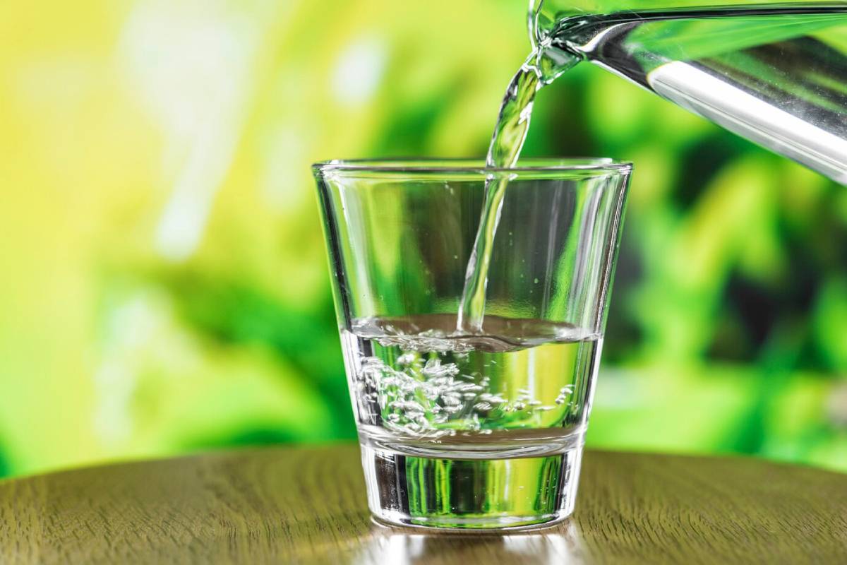 Clear water pouring into a glass on a wooden surface against a green background.