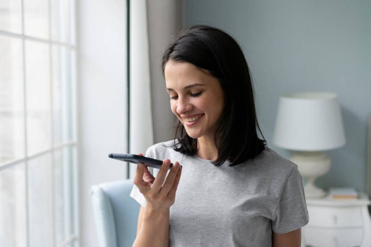 Woman smiling while looking at her smartphone in a bright, cozy room.