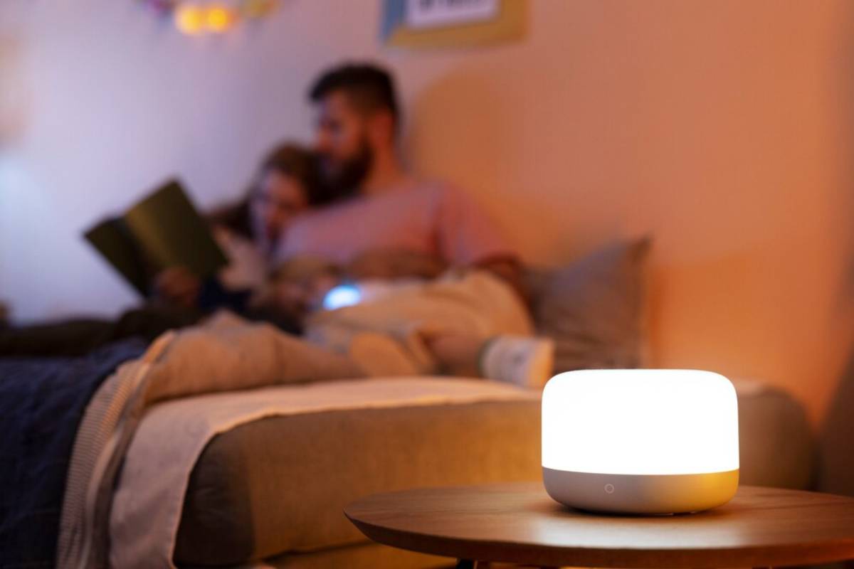 Smart home device on a table, with blurred background of a man and child reading. 