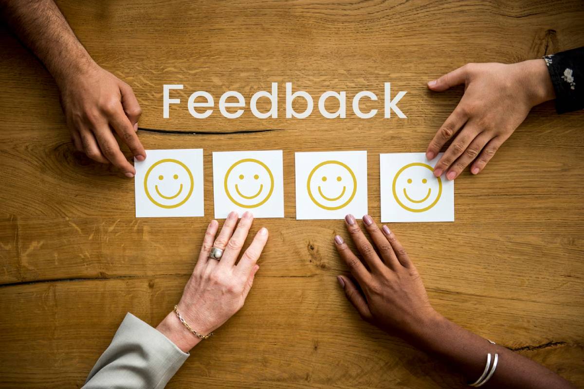 Four diverse hands, each pointing at one of three smiley face cards on a wooden table, above the word