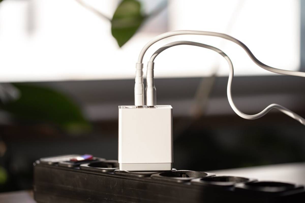   White multi-port USB adapter plugged into a power strip on a desk, with cables connected.