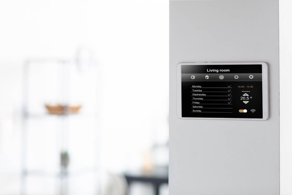 Digital thermostat with a touchscreen display on a wall, showing schedule and temperature settings for a living room. 