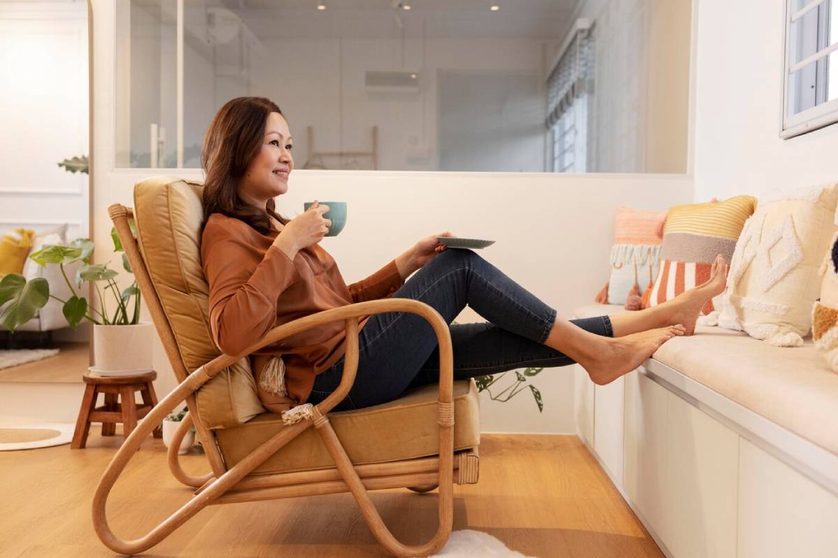  Woman relaxing in a rocking chair with a cup of tea, looking content in a well-lit, cosy living room.