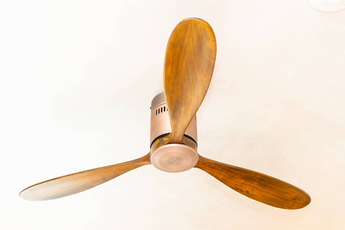 Ceiling fan with three wooden blades mounted on a light-coloured ceiling.
