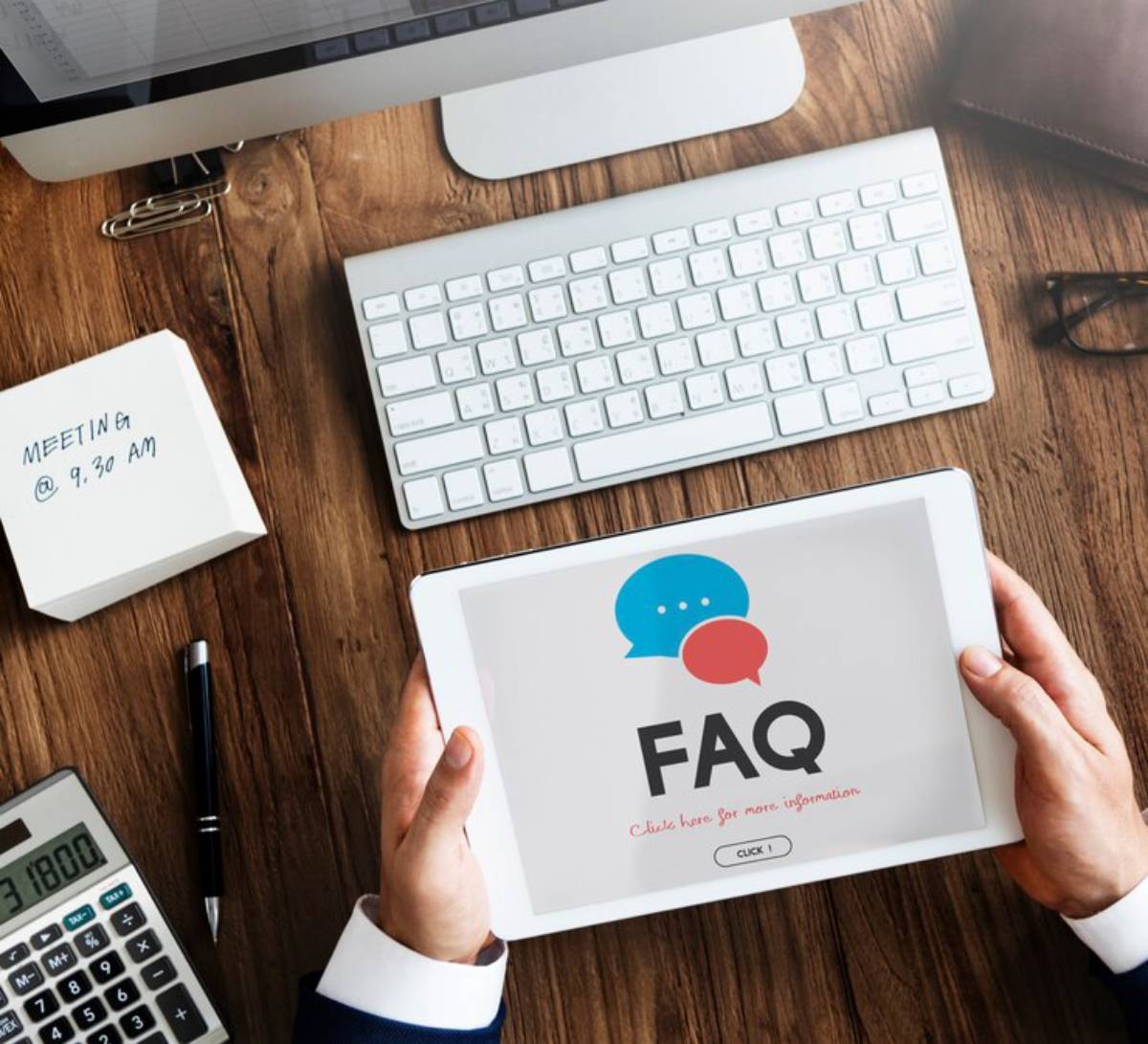 Person holding a tablet displaying an FAQ screen on a busy desk with various office items.