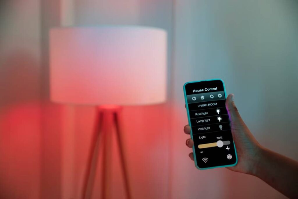 A hand holding a smartphone controlling a smart home lamp with an app interface displayed.