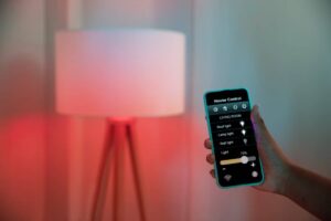 A hand holding a smartphone controlling a smart home lamp with an app interface displayed.