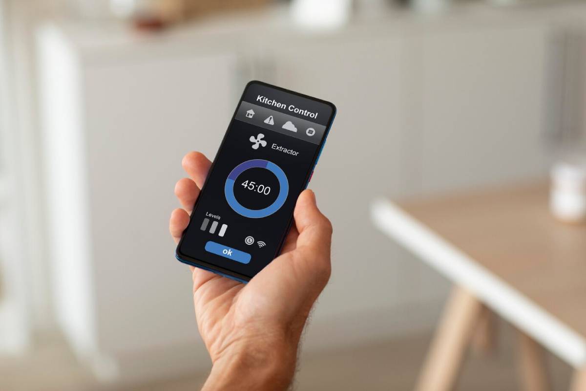 Hand holding a smartphone displaying a kitchen control app with timer and extractor fan settings.