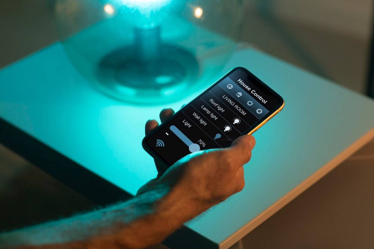Close-up of a hand holding a smartphone controlling home lighting, with an interface visible on the screen.